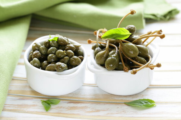 Two kinds of pickled capers in white bowl on wooden table