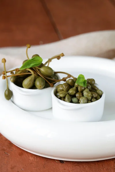 Two kinds of pickled capers in white bowl on wooden table — Stock Photo, Image