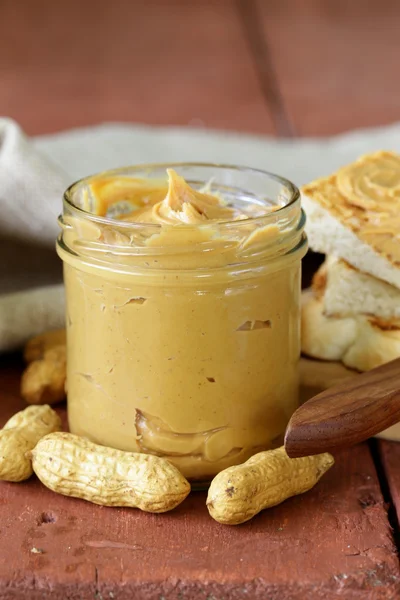Domácí arašídové máslo s celých skořápkových plodů na dřevěný stůl — Stock fotografie