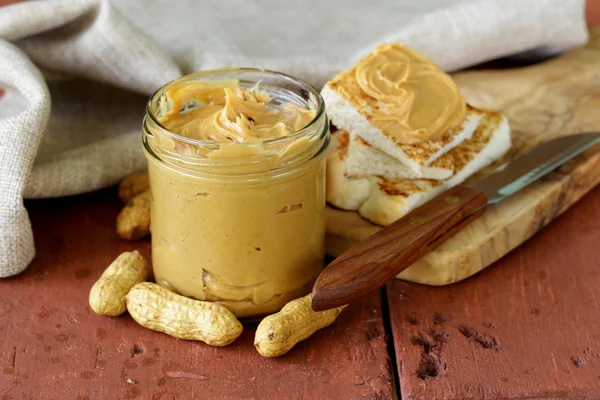 Homemade peanut butter with whole nuts on a wooden table — Stock Photo, Image