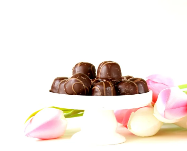 Шоколадные конфеты и цветы на белом фоне — стоковое фото