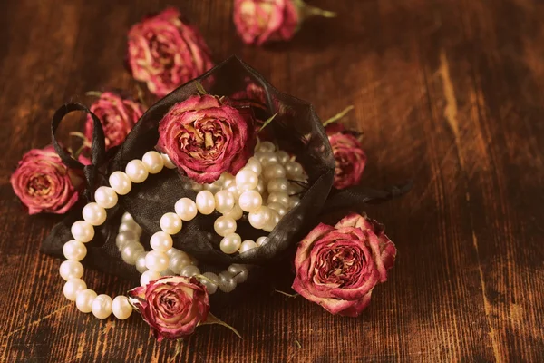 Vintage pearl with dry roses on a wooden background — Stock Photo, Image