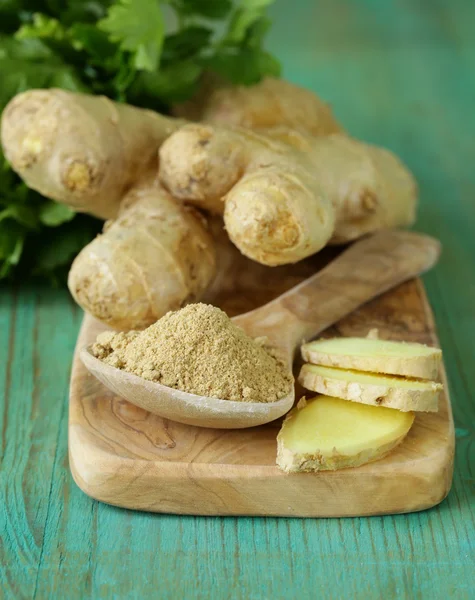 Ground ginger in a wooden spoon, fresh root in the background — Stock Photo, Image