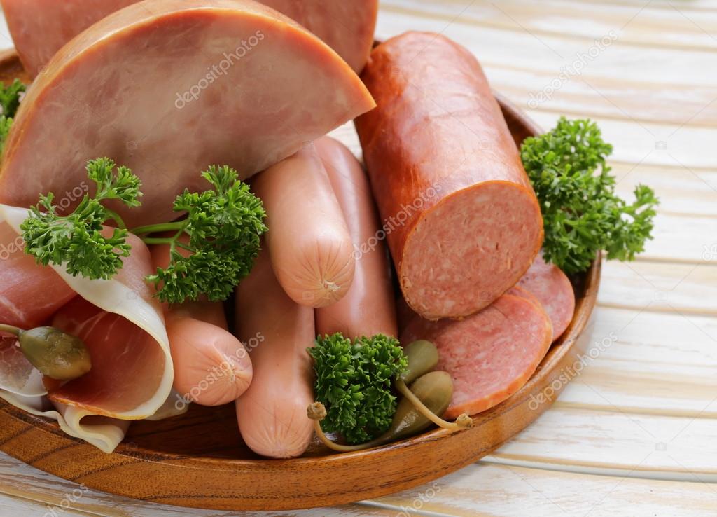 Various kinds of sausages and smoked bacon on the wooden plate