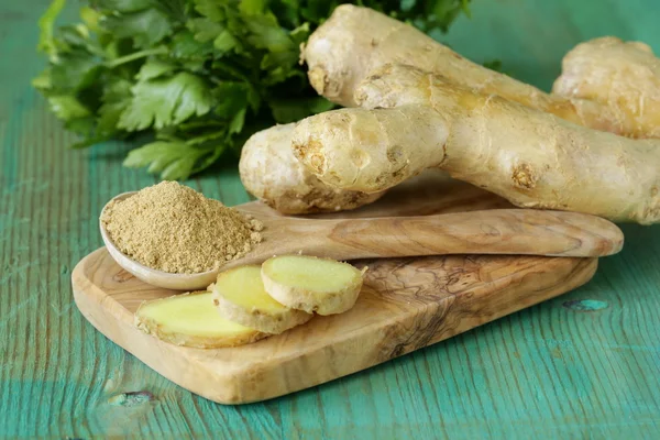 Ground ginger in a wooden spoon, fresh root in the background — Stock Photo, Image