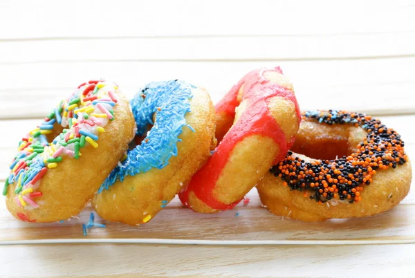 Donuts com esmalte colorido no fundo de madeira — Fotografia de Stock