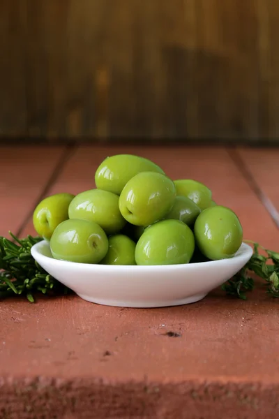 Зеленые оливки в миске на деревянном столе — стоковое фото