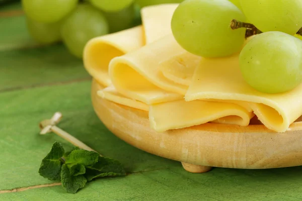 Cheese served on a wooden board with green grapes — Stock Photo, Image