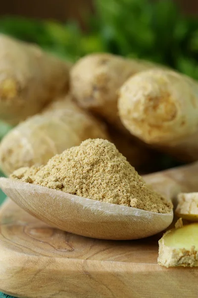 Ground ginger in a wooden spoon, fresh root in the background — Stock Photo, Image