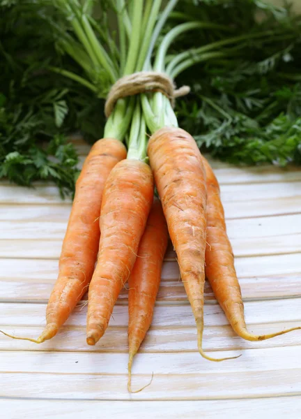 Carottes bio fraîches aux feuilles vertes sur fond bois — Photo