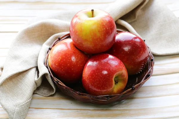 Röda mogna äpplen i en flätad korg på ett träbord — Stockfoto