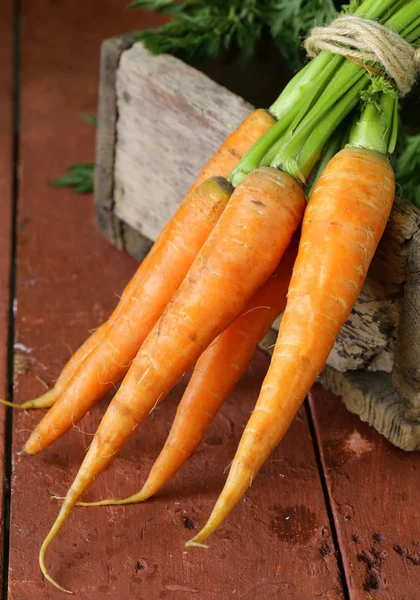 Свіжа органічна морква з зеленим листям на дерев'яному фоні — стокове фото