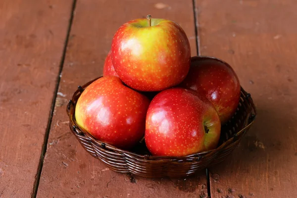 Pommes mûres rouges dans un panier en osier sur une table en bois — Photo