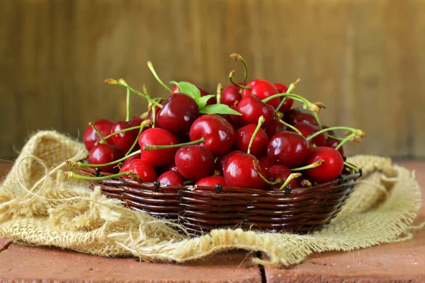 Cerezas frescas rojas maduras en canasta de mimbre sobre una mesa de madera —  Fotos de Stock