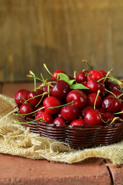 Cerejas maduras vermelhas frescas em cesta de vime em uma mesa de madeira — Fotografia de Stock
