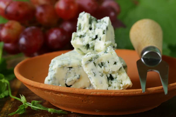 Trozos de queso azul con uvas rojas sobre una mesa de madera — Foto de Stock