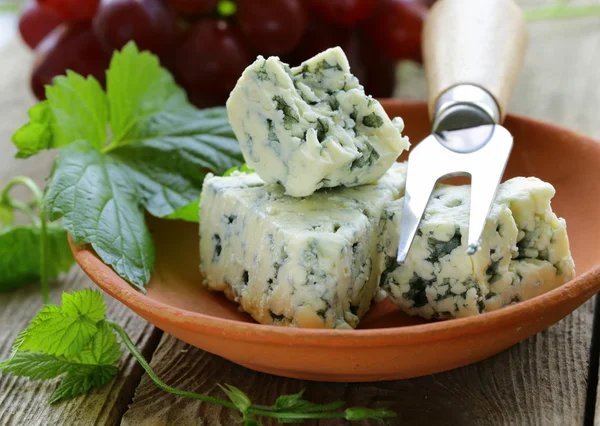 Trozos de queso azul con uvas rojas sobre una mesa de madera — Foto de Stock