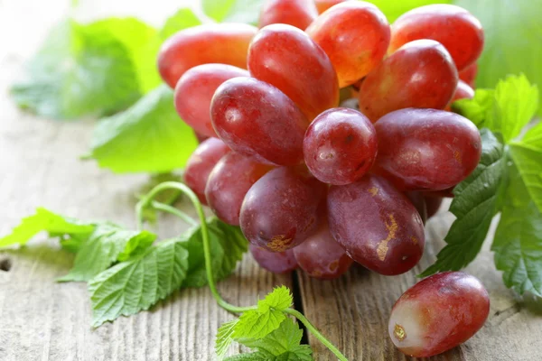 Oddział czerwony dojrzałe winogrona z zielonych liści na drewnianym stołem — Zdjęcie stockowe