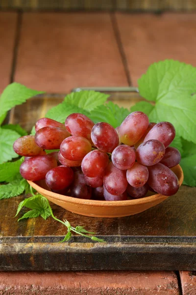 Ветвь красного спелого винограда с зелеными листьями на деревянном столе — стоковое фото