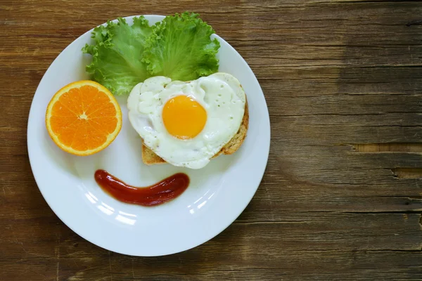 Funny face serving breakfast, fried egg, toast and green salad — Stock Photo, Image