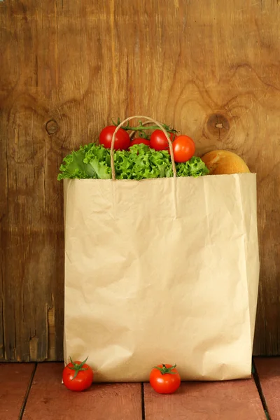 Papiertüte mit Lebensmitteln, Salat, Tomaten, Brot auf Holzgrund — Stockfoto