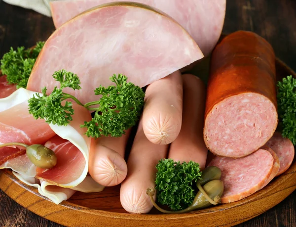 Various kinds of sausages and smoked bacon on the wooden plate — Stock Photo, Image