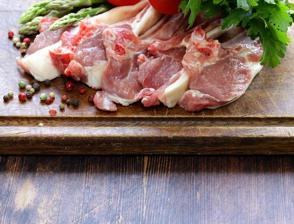 Carne cruda, chuletas de cordero con verduras sobre tabla de madera —  Fotos de Stock