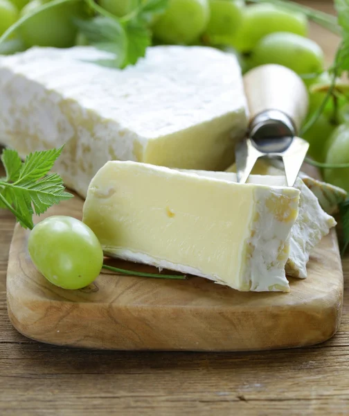 Soft brie cheese with sweet grapes on a wooden board — Stock Photo, Image