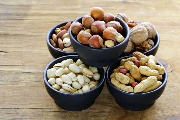 Verschiedene Arten von Nüssen (Mandeln, Walnüsse, Haselnüsse, Erdnüsse) in einer Schüssel auf einem Holztisch — Stockfoto