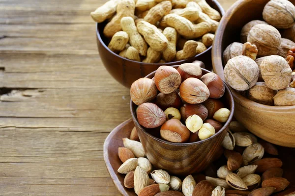 Different kinds of nuts (almonds, walnuts, hazelnuts, peanuts) in a bowl on a wooden table — Stock Photo, Image
