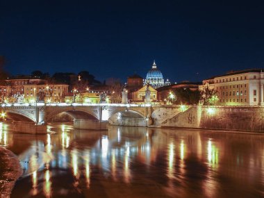 Ön planda Tiber nehri üzerinde bir köprü ve Vatikan 'da Aziz Peter Bazilikası ile Roma' nın genel gece manzarası