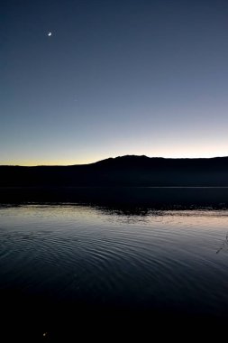Gökteki ay, gün batımının mavi saatinde İspanya 'daki Sanabria Gölü' ndeki suya yansıyordu.
