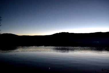 Gökyüzünde parlayan gezegen, gün batımında, İspanya 'nın Sanabria Gölü' ndeki suya yansıyan dağların siluetinin üzerinde.