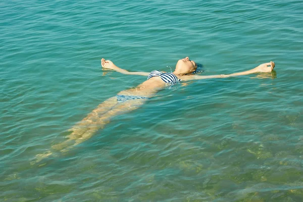 Tiener meisje liggend op het wateroppervlak zee — Stockfoto