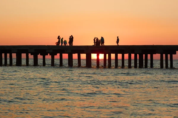 Människor på den gamla piren i havet under solnedgången — Stockfoto