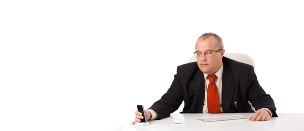 Zakenman aan bureau zitten en houden een mobilephone met werkrug — Stockfoto