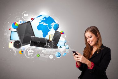 Genç bir kadın ayakta ve telefonunda geziniyor.