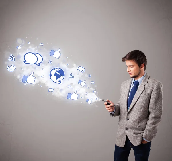 Attractive young man holding a phone with social media icons — Stock Photo, Image