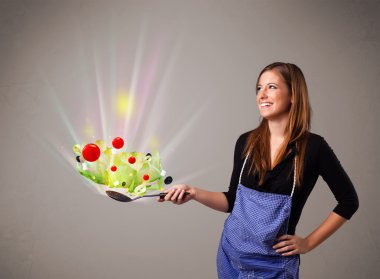 Genç bir kadın taze sebze pişiriyor.