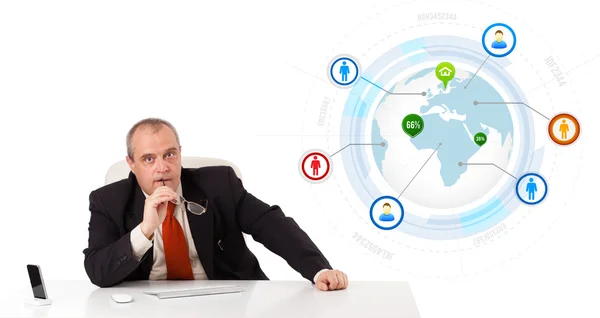 Businessman sitting at desk with a globe and social icons Royalty Free Stock Photos