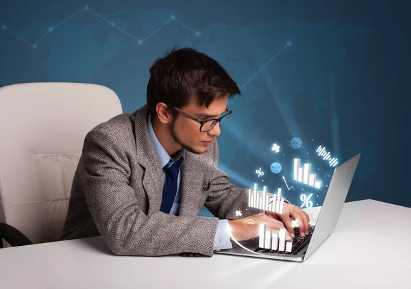 Young man sitting at desk and typing on laptop with diagrams and — Stock Photo, Image