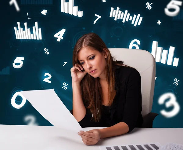 Young businesswoman sitting at desk with diagrams and statistics — Stock Photo, Image