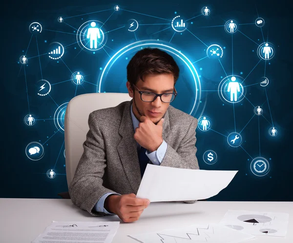 Businessman sitting at desk with social network icons — Stock Photo, Image