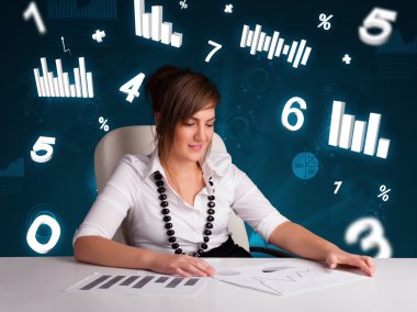 Masasında şema ve istatistiklerle oturan genç iş kadını.