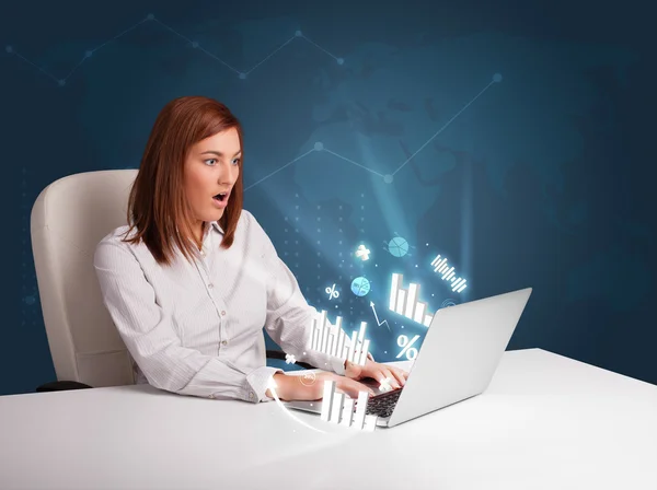 Pretty woman sitting at desk and typing on laptop with diagrams — Stock Photo, Image