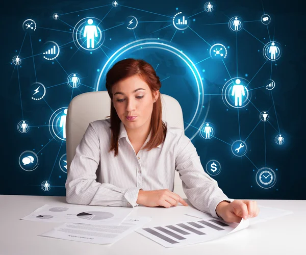 Businesswoman sitting at desk with social network icons — Stock Photo, Image