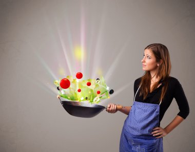 Genç bir kadın taze sebze pişiriyor.