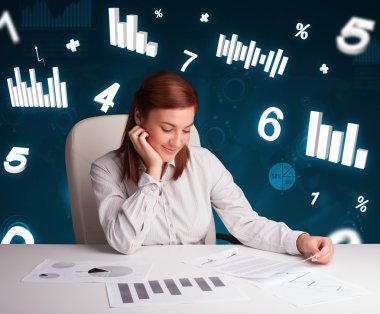 Masasında şema ve istatistiklerle oturan genç iş kadını.