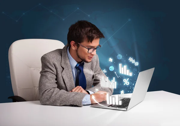 Junger Mann sitzt am Schreibtisch und tippt auf Laptop mit Diagrammen und — Stockfoto