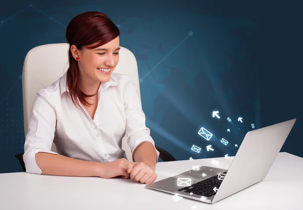 Mladá dáma sedí u dest a psaní na notebooku s zprávy ico — Stock fotografie